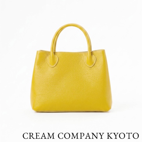 這是一款由 CREAM COMPANY KYOTO 出品的黃色皮革手提托特包，包身採用質感柔軟的牛皮製作，表面呈現細膩的荔枝紋理，設計簡約優雅，配有圓弧型提把，包底寬闊立體，整體呈現亮眼且具有職人手作感的精緻外型。