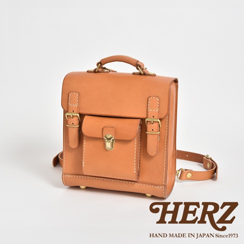 職人手作皮革經典學院風迷你後背包，採用天然皮革製成，呈現焦糖棕色。包款設有翻蓋、金屬扣環與調節式皮帶，設計簡約而實用。