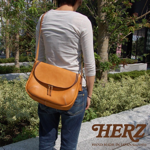 日本HERZ手工皮革大容量馬鞍側背包，採用橘棕色Stare皮革製作，配有雙拉鍊主袋和可調式長背帶，展現職人手作質感。