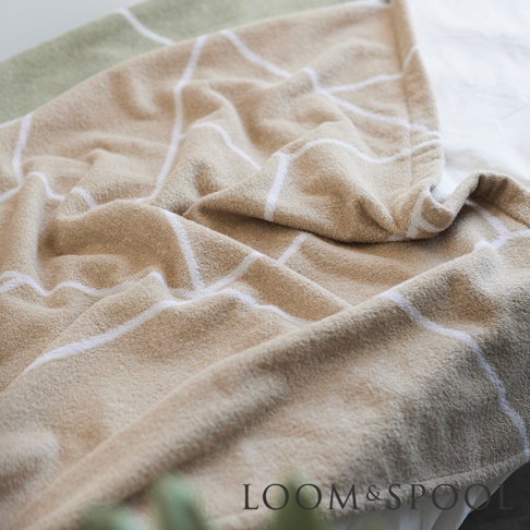 淺棕色純棉毛巾，帶有白色幾何線條圖案，一角為淺綠色，近距離拍攝，展示其柔軟觸感。