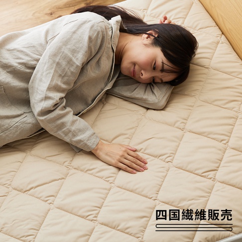 雙人加大羊毛床墊，採用菱格紋縫製，色調為溫暖的米白色，表面觸感柔軟。一位女性正側臥於床墊上，手部輕觸床墊表面。