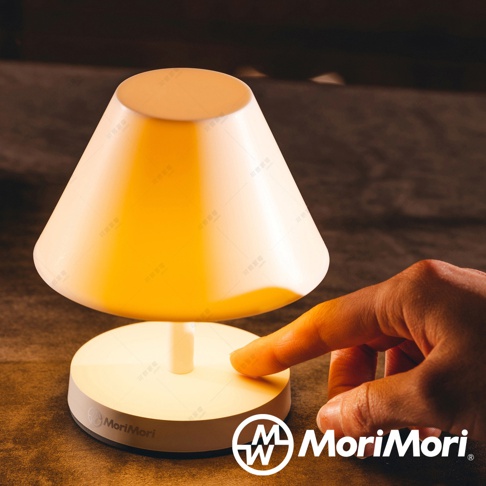 一盞帶有傘型燈罩的白色LED檯燈，燈罩為乳白色，底座也是白色，燈光呈現溫暖的黃色。一隻手指正按下底座中央的按鈕。