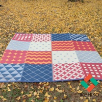 一張防水 PP 戶外室內兩用收納野餐墊，表面由多個不同圖案的方塊拼接而成，包含網格、圓點、鋸齒紋、菱形紋、幾何圖案等，色彩豐富，有紅、藍、白、黃等色調，鋪設在落葉的草地上。