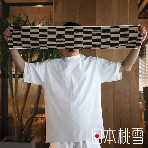 一位身穿白色T恤的人手持一條有黑白格紋的毛巾，毛巾上有日本桃雪的標誌。
