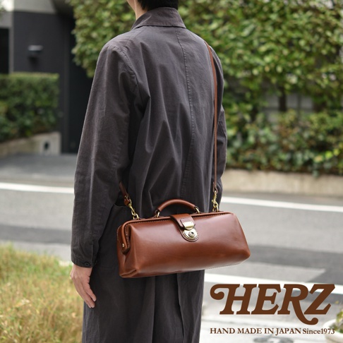 日本HERZ 職人手作皮革橫長形杜勒斯單肩包，深棕色皮革，由後方視角展示，包款帶有復古醫生包造型，印有HERZ HAND MADE IN JAPAN Since1973 字樣。