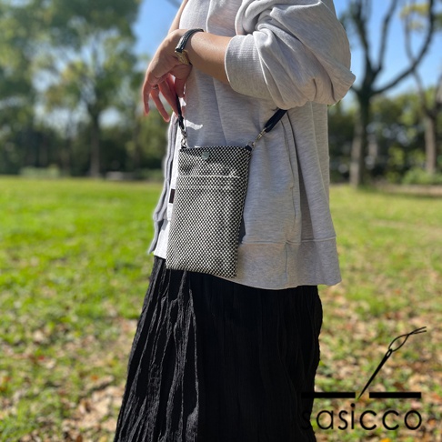 一名女性身穿灰色連帽衫和黑色長裙，斜挎一個黑白格子圖案的三河木綿刺子織手機包。