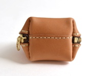 一個棕色皮革製成的貝殼造型零錢包，兩側有黃銅拉鍊，縫線為米白色，呈現簡約復古風格。