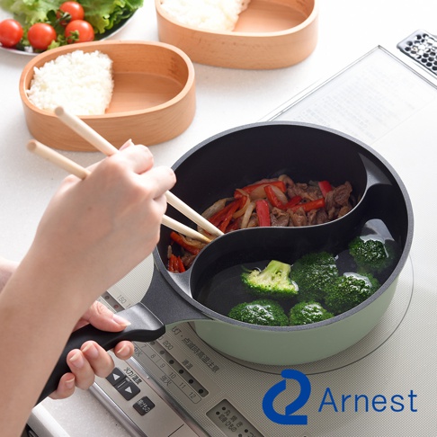 Arnest 鴛鴦料理鍋，一手用筷子夾取鍋中炒肉與蔬菜，另一手控制鍋柄，鍋中分隔成兩側，一側煮著牛肉與紅椒，另一側煮著青花菜。