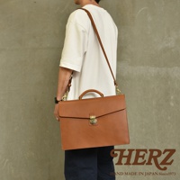 職人手作皮革Organ兩用商務公事包，採用光滑的棕色皮革製成，配有頂部提把和可拆卸肩帶，正面設有旋轉鎖扣，適合商務場合使用。