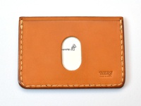 職人手作皮革橫式票券收納夾，採用棕褐色皮革製成，正面中央有橢圓形透明視窗，右下方壓印有「HERZ MADE IN JAPAN」字樣，邊緣以白色縫線手工縫製。