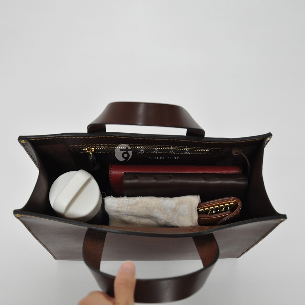 職人手作皮革直式托特包 T-44 S，深棕色，內部裝有白色圓形物品、紅色與棕色皮夾、布包及鑰匙包。