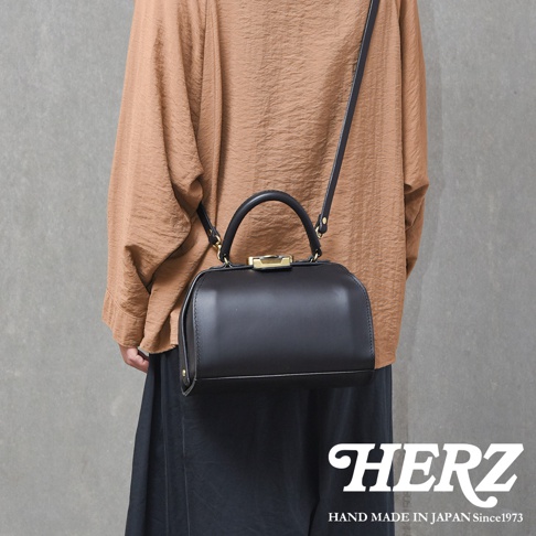 黑色職人手作皮革Organ兩用口金手提包，包身線條圓潤，配有金色口金鎖扣與提把，可肩背或手提。