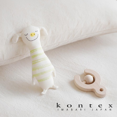 白色有機棉抓握玩偶，帶有綠色條紋，造型像可愛的動物，臉部有黑色線條繡出的眼睛和嘴巴，黃色鼻子。旁邊有一個淺木色的木製搖鈴。