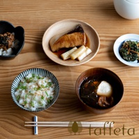 一張木質餐桌上擺放著日式早餐，包含烤魚、納豆、飯、味噌湯和配菜，旁邊有木筷子。