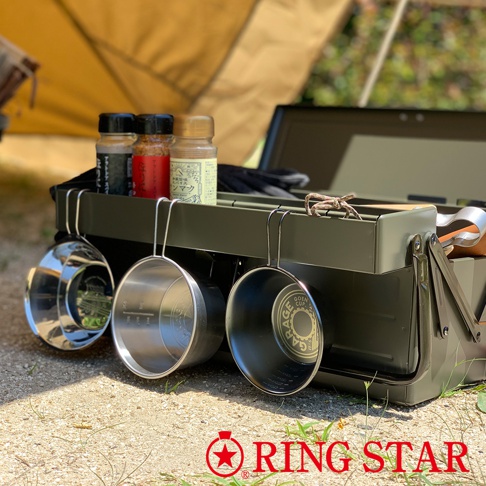 軍綠色金屬工具箱，附有三個掛勾，上面掛著三個不同顏色和材質的杯子，分別是閃亮的銀色金屬杯、啞光銀色金屬杯和黑色金屬杯。箱子上方擺放著三個調味料瓶，其中一個瓶子標示著日文。