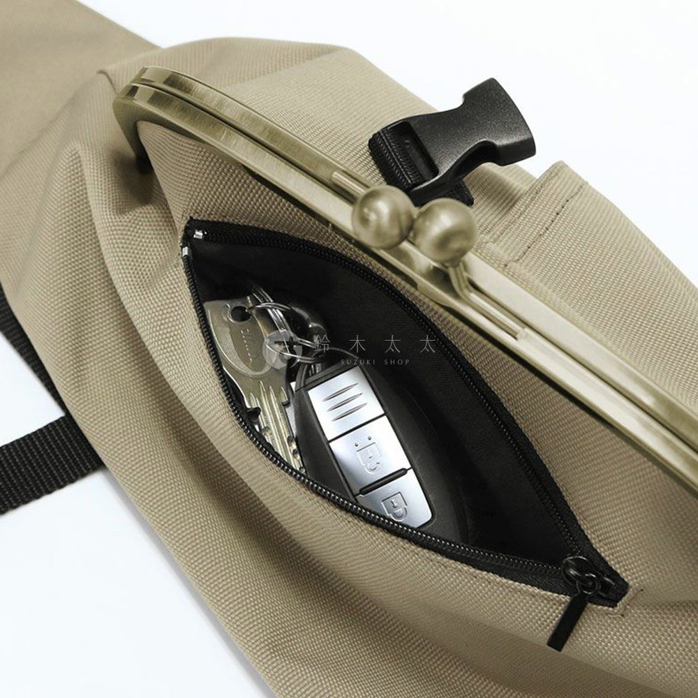 近距離特寫，展示一個卡其色布質斜背包側面，拉鍊打開後可見一串鑰匙和汽車鑰匙，背包上有金屬扣和兩個圓球裝飾。