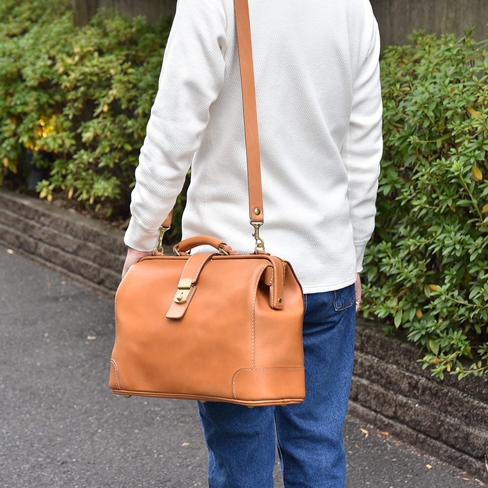 職人手作皮革商務旅行兩用公事包，採用天然棕色皮革，配有金色鎖扣和可拆卸肩帶，適合日常或商務場合。