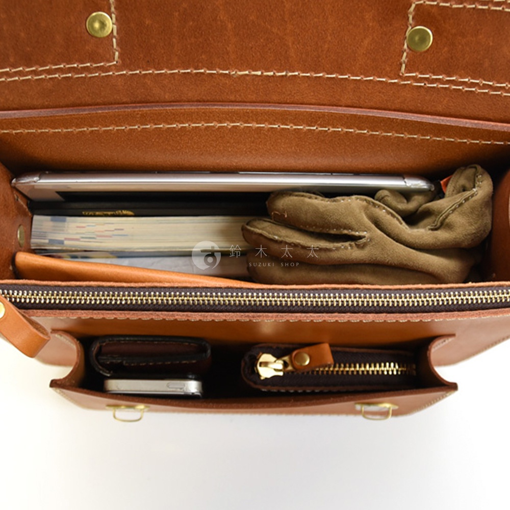 棕褐色皮革製成的單肩包內部，展示著手機、書本、手套、錢包和零錢包。