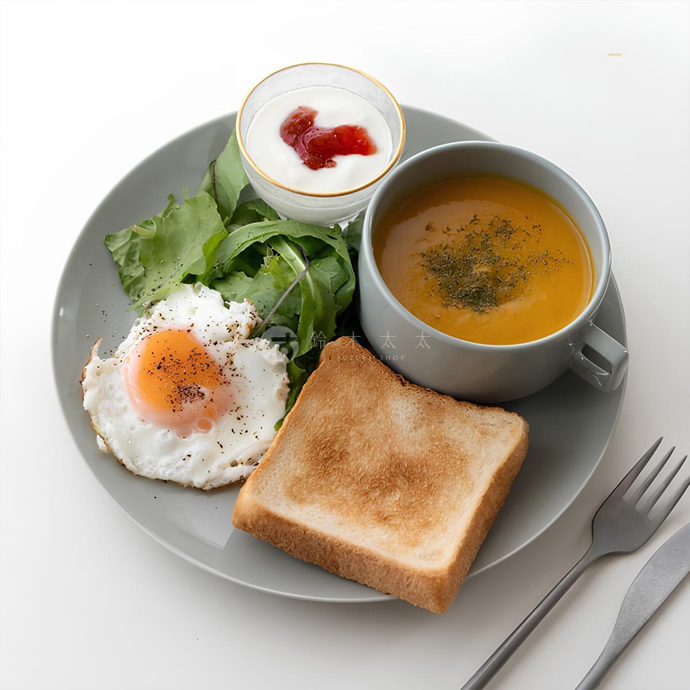 灰色美濃燒圓盤上盛有早餐：煎蛋、吐司、蔬菜沙拉、南瓜濃湯及優格杯，搭配灰色餐具。