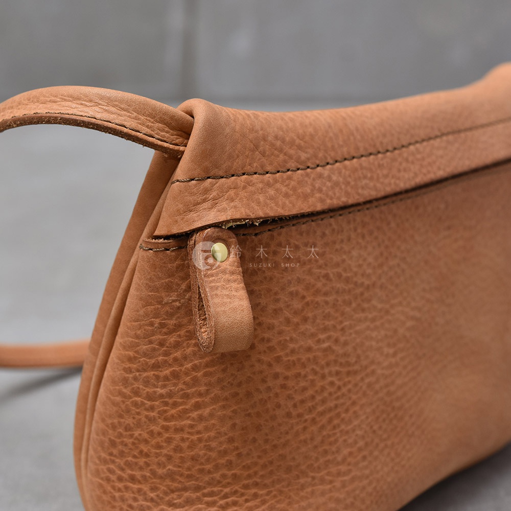 皮革斜背包的細節，包含拉鍊頭和肩帶。