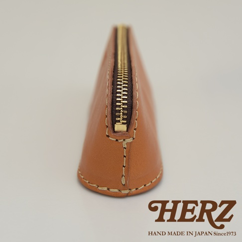 職人手作皮革三角弧形收納筆袋，採用棕褐色皮革製成，設有金色拉鍊。