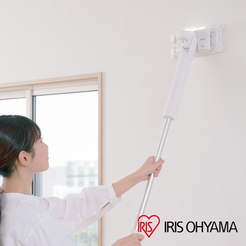 一位女性正使用白色機身、銀色金屬握桿的電動平板拖把清潔牆面。拖把頭為透明方形，裝有白色清潔墊，並有LED燈照明。