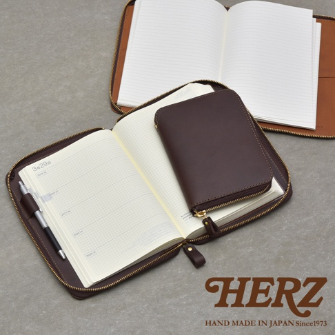 職人手作皮革Organ記事本收納包，深棕色，打開的狀態，內有筆記本和一支筆，下方有HERZ品牌標誌