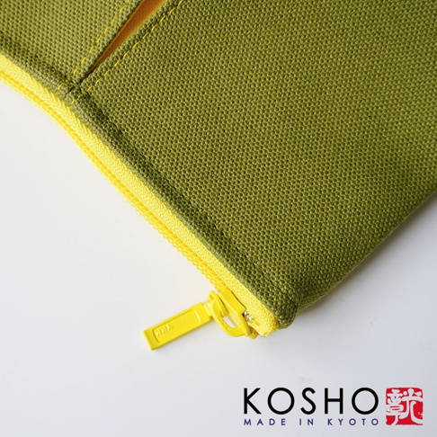 一張特寫鏡頭顯示京都KOSHO ougi系列帆布化妝收納包的細節，包身採用橄欖綠色帆布材質，搭配亮黃色的拉鍊與金屬拉鍊頭，邊緣車縫線工整細緻，右下方印有KOSHO MADE IN KYOTO的黑色品牌名稱與紅色印章標誌。