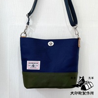 犬印純綿帆布雙色迷你側背包，主體為海軍藍，底部為軍綠色，配備可調節的深藍色織帶肩帶，銀色金屬扣具，正面有品牌標籤和金屬旋轉鎖扣。