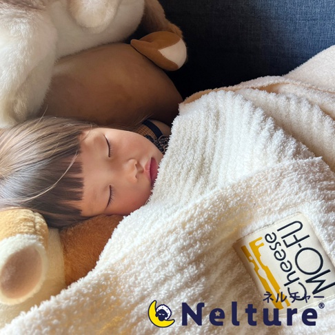 嬰兒蓋著柔軟的米白色毛毯，毛毯上印有「MO-FU Cheese」的字樣及起司圖案。