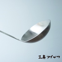 金屬光澤的不鏽鋼湯勺，勺頭呈圓弧形，勺柄細長，背景為淺藍色調。