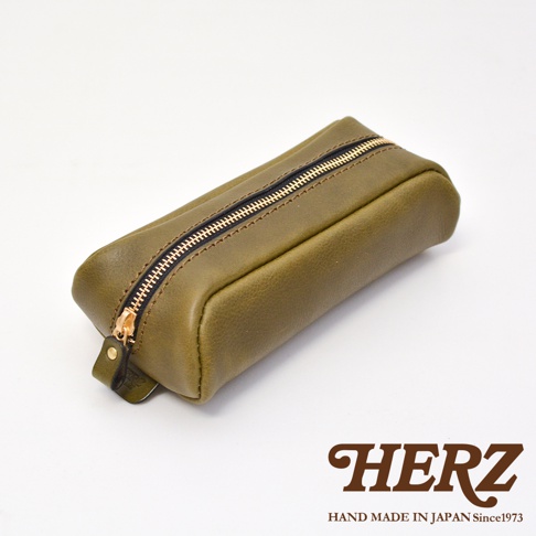 這是一個由日本 HERZ 職人手工製作的橄欖綠色皮革筆袋，採用圓角長方形設計。筆袋正面配有金色拉鍊，拉鍊頭裝飾皮革拉環，整體風格簡約復古，底部印有 HERZ 手作皮革品牌標誌。