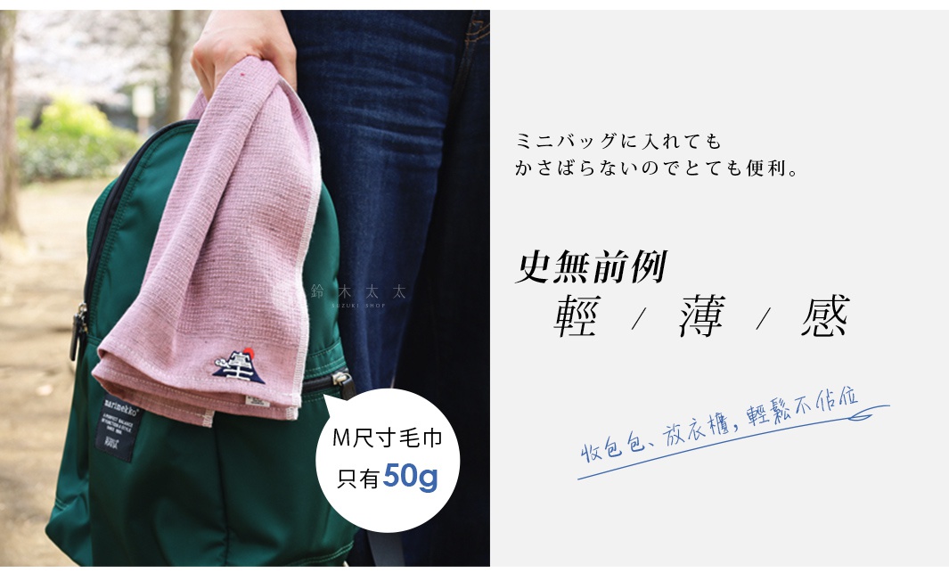 一條粉色輕薄吸水長毛巾，繡有富士山圖案，掛在深綠色背包上。