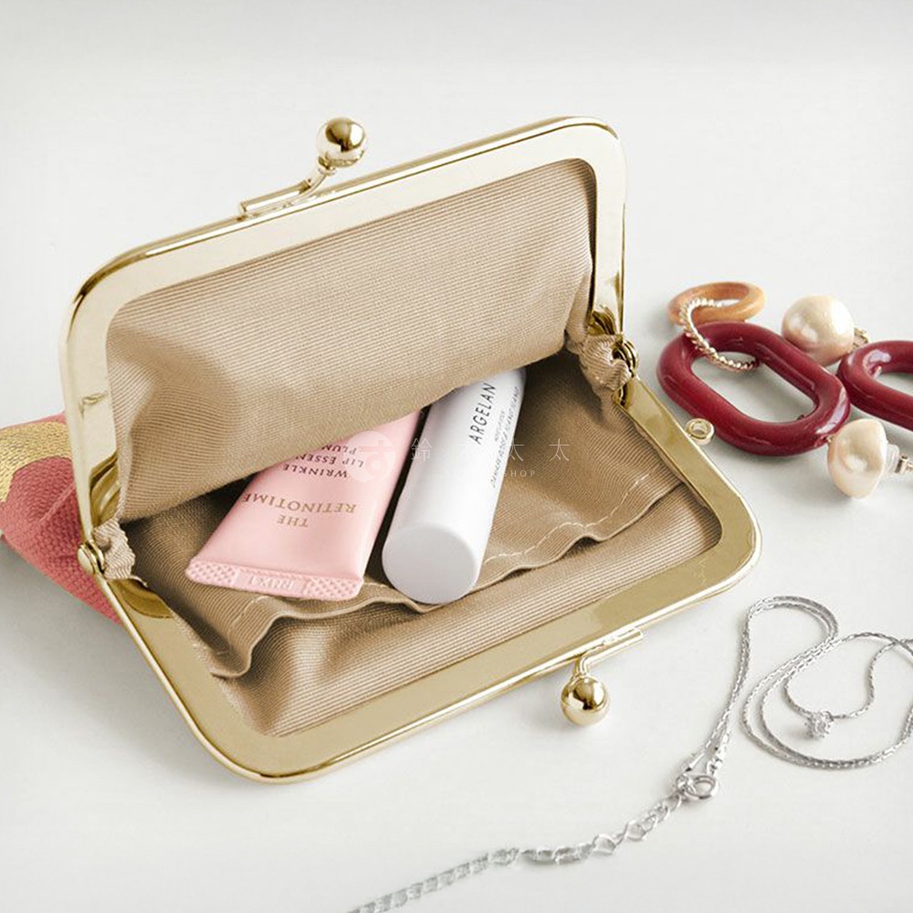 金色的口金包內有粉色的唇部精華和一根白色管狀物，旁邊散落著一串項鍊和一組琥珀色的飾品。