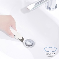 手持白色萬用去污橡皮擦，其深灰色海綿狀去污端正靠近白色水槽的排水孔，水槽為陶瓷材質，上方有鉻合金水龍頭。