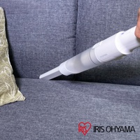 白色手持無線吸塵器，配有透明集塵筒，正在清潔灰色布藝沙發的縫隙。