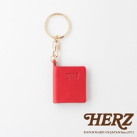 紅色皮革書本造型鑰匙圈，附金色金屬環及鉤扣，書本上壓印有「HERZ」及「MADE IN JAPAN」字樣。