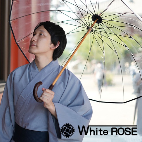 一位身著灰色和服的男子撐著一把透明傘，傘骨為黑色，傘柄為木質。