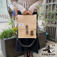 犬印純綿帆布三用直式側背包，淺褐色帆布主體，搭配棕色皮革飾邊與皮帶扣，正面有兩個小皮質插槽，左側有品牌標籤。