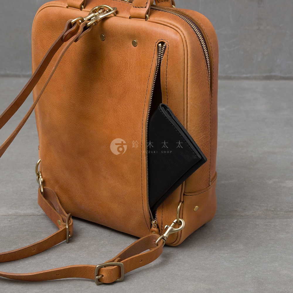 職人手作皮革Organ商務後背包 M-10，一個黑色皮夾從側邊拉鍊口袋露出，背包為棕褐色皮革材質，配有金屬釦環和皮質揹帶。
