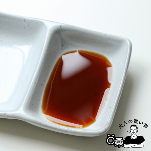 一個淺灰色的陶瓷沾醬碟，其中一格裝有深棕色的醬料，碟面有細小的黑色斑點。