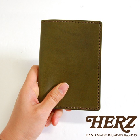 一只手拿著橄欖綠的皮革經典護照套，其邊緣有縫線裝飾。