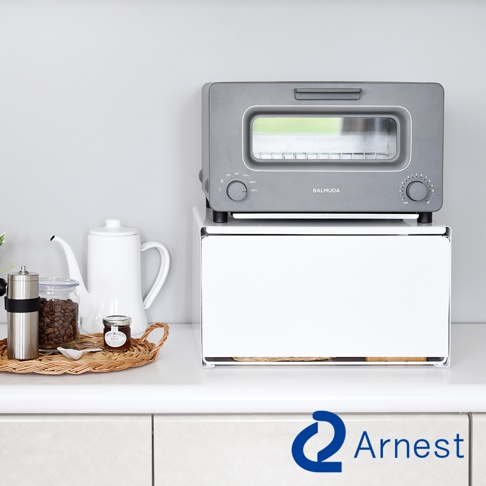 白色多功能收納架上放置著一個灰色小烤箱，收納架下方及烤箱旁有餐具、咖啡豆罐、果醬罐和白色水壺。