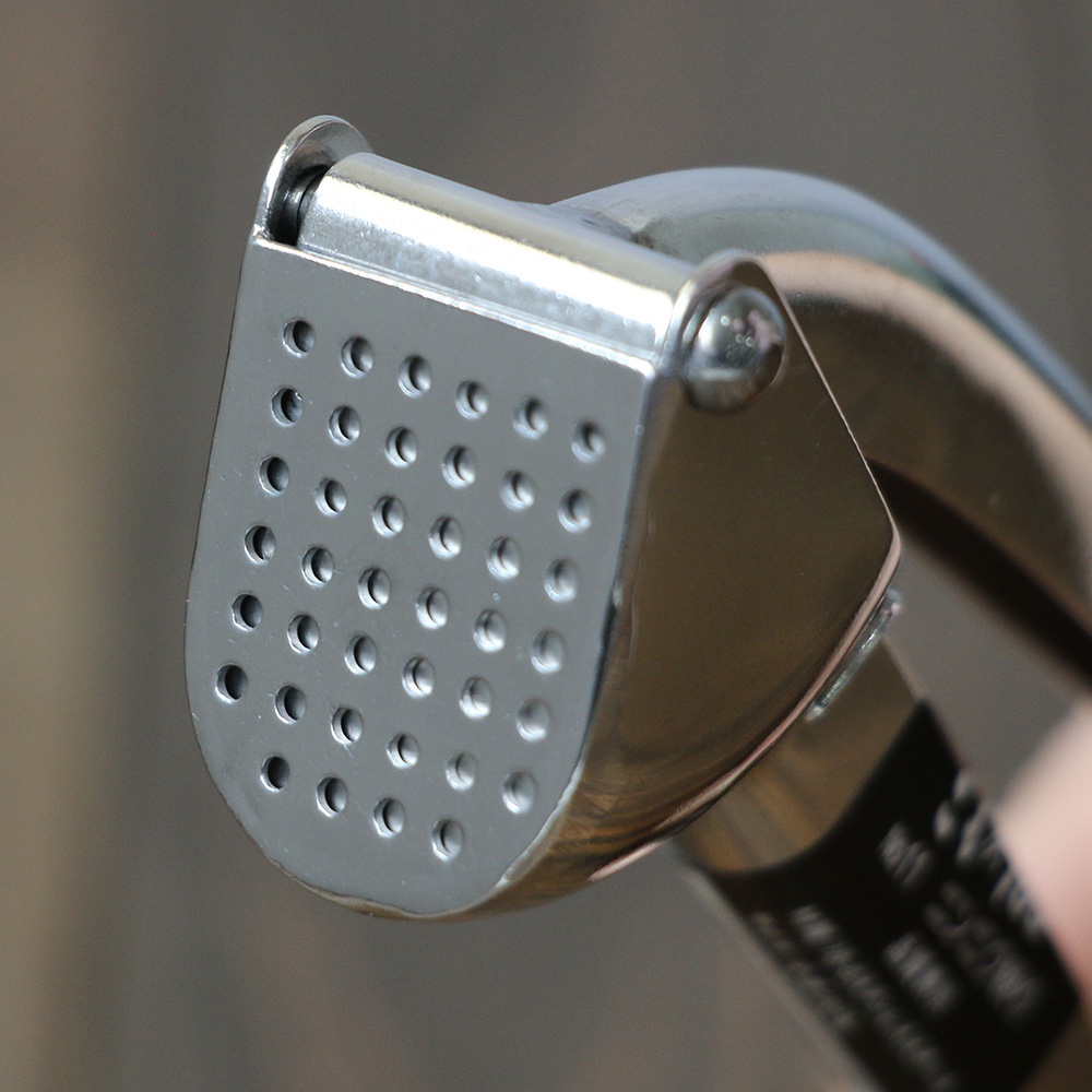 不鏽鋼壓蒜器，帶有圓形孔的壓板，整體為銀色金屬材質，結構緊湊，設計簡潔。