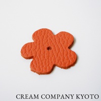 橘色皮革製成，五瓣花朵造型吊飾，表面帶有壓紋，中央有圓形孔洞。