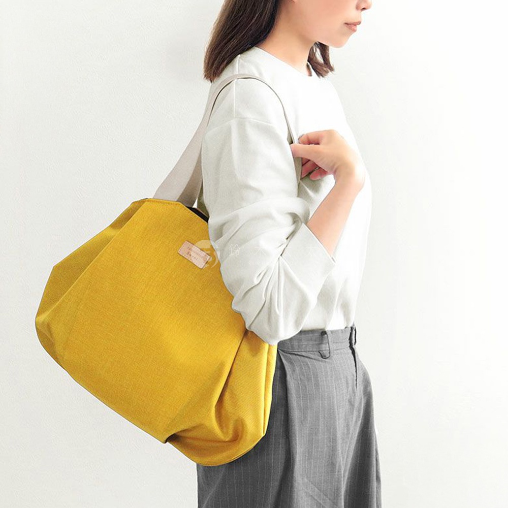 一位身穿白色上衣和灰色條紋長褲的女性，斜揹著一個亮黃色的托特包