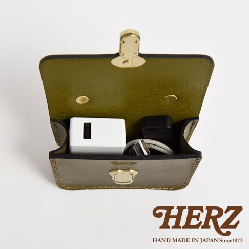 職人手作皮革迷你收納包，呈現橄欖綠色，內部裝有白色USB充電器、黑色轉接頭及USB充電線。包包採用金屬釦環開合，邊緣有精緻縫線。