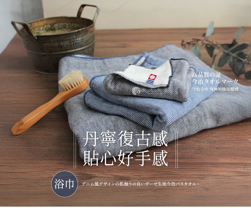 今治復古丹寧風雙織柔感浴巾，呈現藍色與灰色調，疊放展示，其中一條浴巾有白色織標，搭配木柄毛刷和復古金屬水桶。