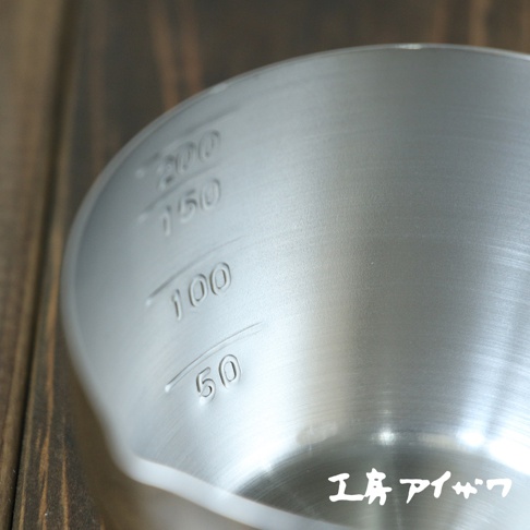 不鏽鋼長柄量杯，內側刻有50ml、100ml、150ml、200ml的刻度，材質呈現銀色金屬光澤，置於木紋背景上。