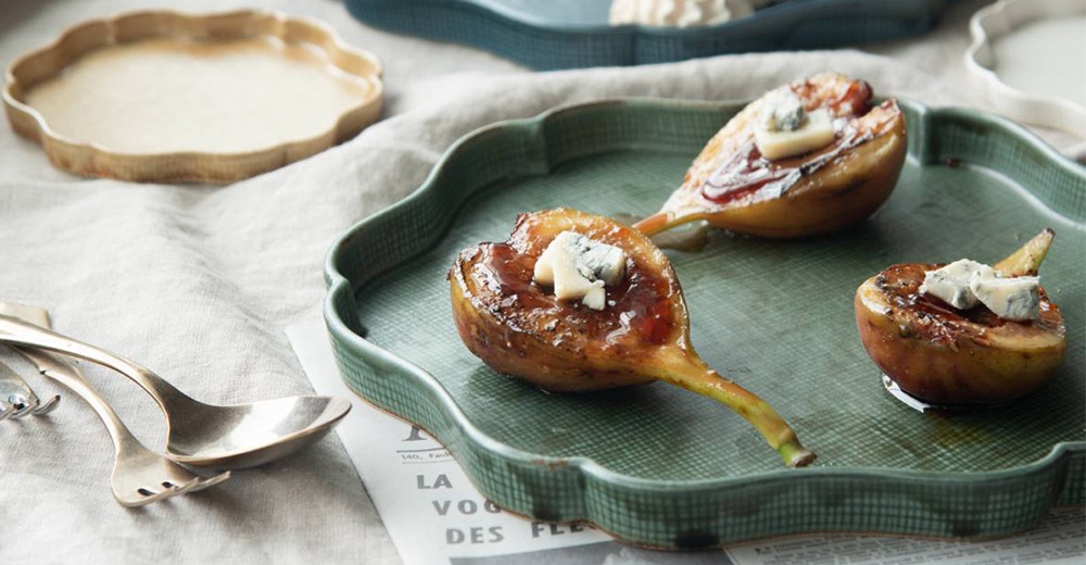 綠色美濃燒花型主食盤，盤中盛有烘烤過的無花果，撒有起司和糖漿。盤子邊緣帶有細緻的紋理，整體呈現日式風格。